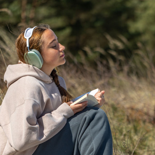 Teenage girl reading a book outdoors. Reading a book and listening to music. High quality photo. Space for text. Student preparing for exams outdoors.